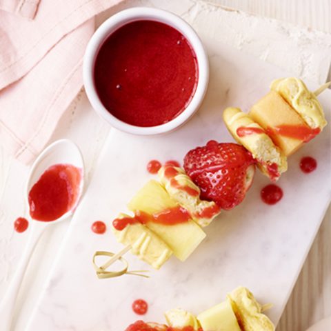 Plated fruit kebabs with a side of raspberry puree.